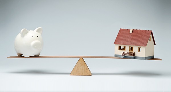 Picture of a piggy bank and house on a balance beam.