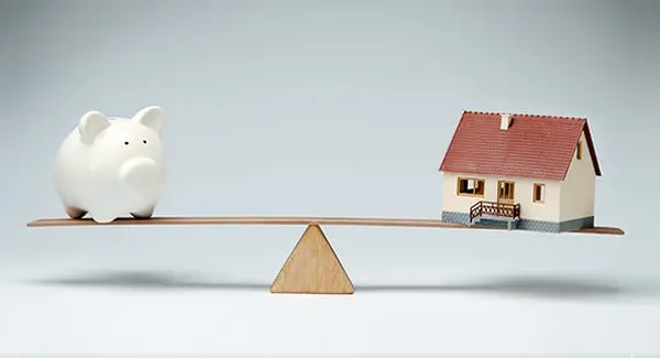 a piggy bank and house on a balance beam.