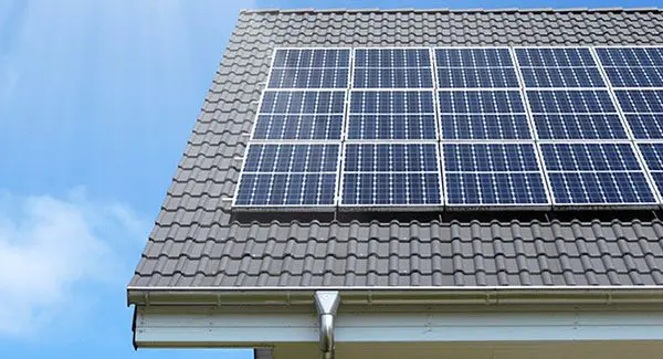 Rooftop solar panels mounted on a gray tiled roof under a clear blue sky.
