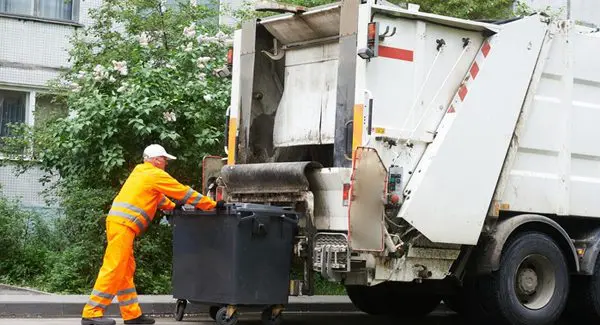 a garbage man putting trash into his truck.
