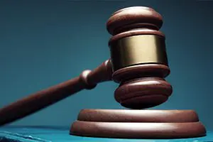 A wooden judge’s gavel rests on a sound block, symbolizing law and legal proceedings, against a dark blue background.