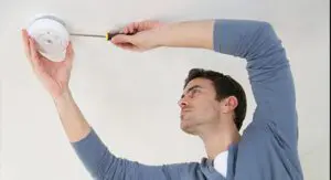 A person uses a screwdriver to install or check a smoke detector on a white ceiling.