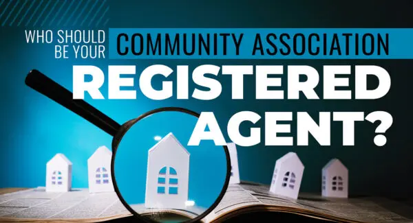 A magnifying glass focuses on a paper house model, with the text "Who should be your community association registered agent?" in the background.