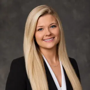 Headshot of a smiling woman with long blonde hair wearing a black blazer and white top.