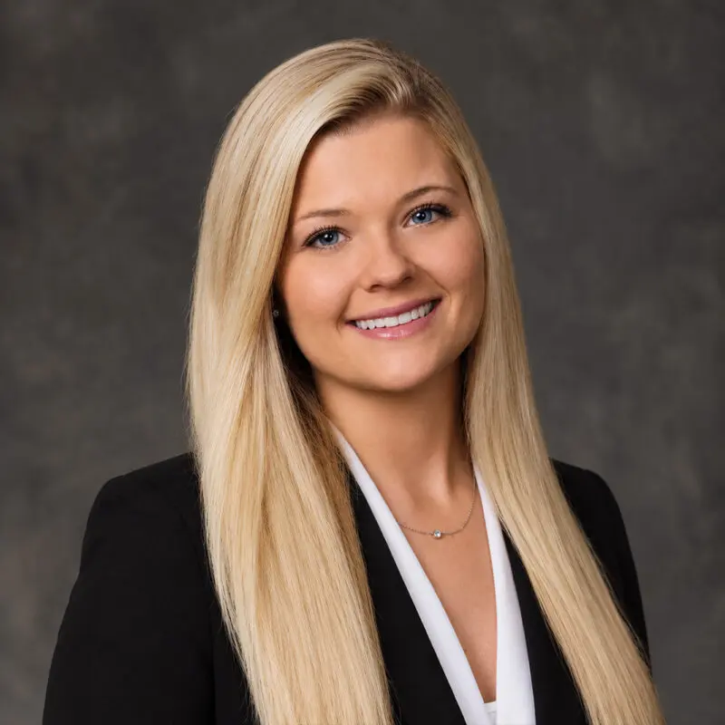 Headshot of a smiling woman with long blonde hair wearing a black blazer and white top.