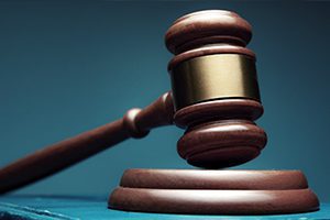 A wooden judge’s gavel rests on a sound block, symbolizing law and legal proceedings, against a dark blue background.