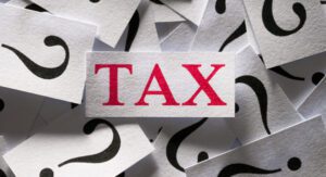 A card with the word "TAX" in red letters is surrounded by cards featuring black question marks.